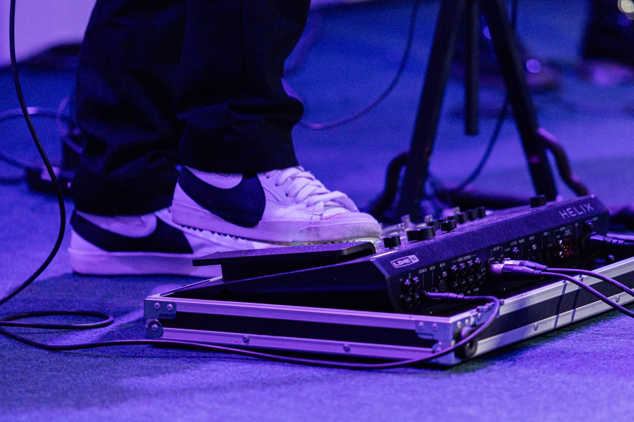 Close-up of a musician's foot on a guitar effects pedal with vibrant stage lighting.